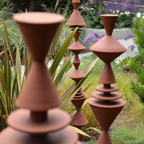 Garden Cones sculptures, composed from modular handmade pieces, are at home both indoors and out. With a nod to mid-century modern, the geometric forms repeat playfully, complementing both plants and architecture. 60 inches tall, terra cotta or white stoneware, pottery decor.